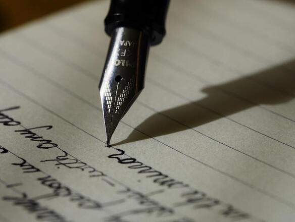 A ghostwriter's black fountain pen writes cursive lettering on lined paper.