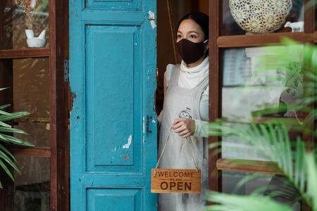A female business owner holds an open sign and wears a mask due to the COVID-19 pandemic
